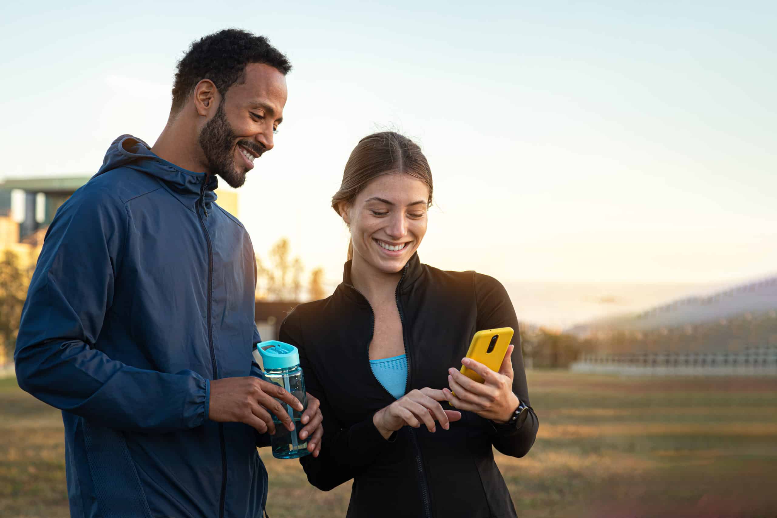Multiracial couple checking fitness app on mobile phone after working out outdoors. Couple looking phone. Copy space. cryolipolyse